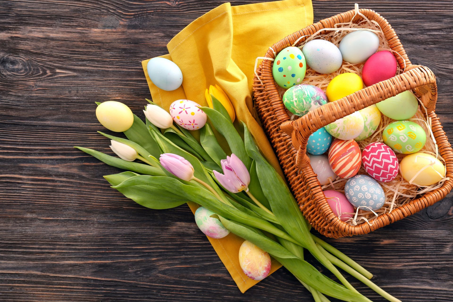Easter basket with colorful eggs and spring flowers on wooden background, top view