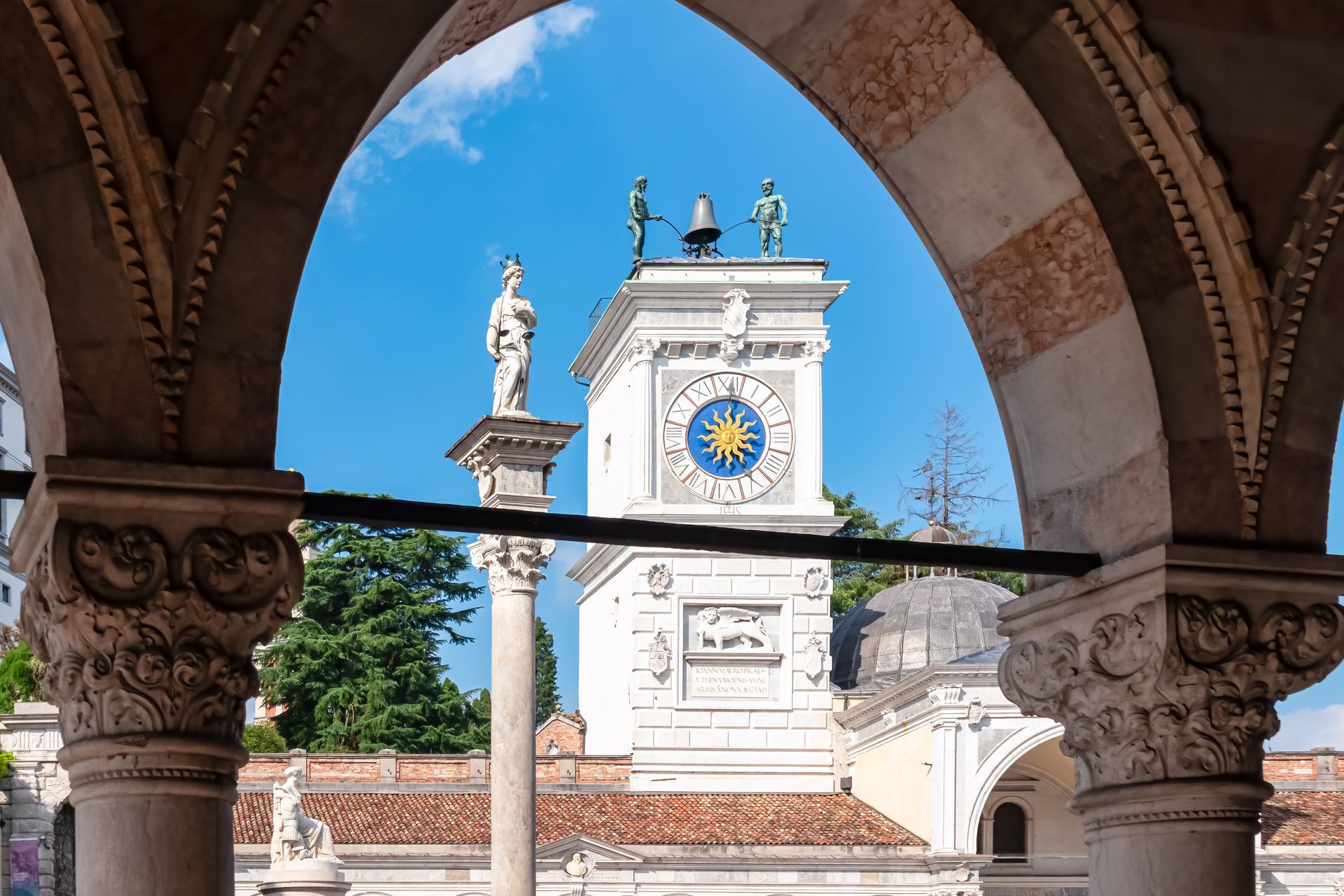 Columns of Loggia del Lionello with scenic view of Venetian style clock tower Torre dell'Orologio on main square Piazza della Liberta in historic old town Udine, Friuli Venezia Giulia, Italy, Europe
